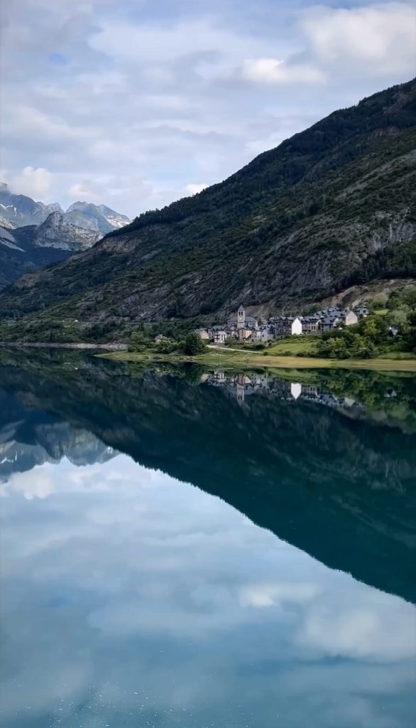 Vista panorámica del lago de Lanuza con el pintoresco pueblo en el fondo, rodeado de montañas en los Pirineos.