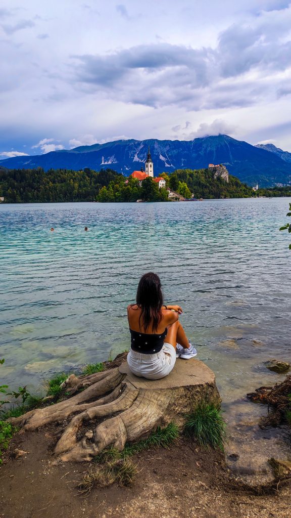 Chica snetada de espaldas mirando la isla central del Lago Bled y los alpes al fondo