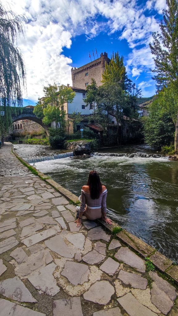 Chica a orillas del río en Potes con su puente y castillo al fondo